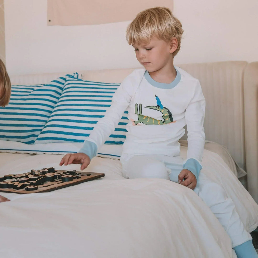Young boy in white pajamas from Firebird Kids with playful animal print sitting on a bed