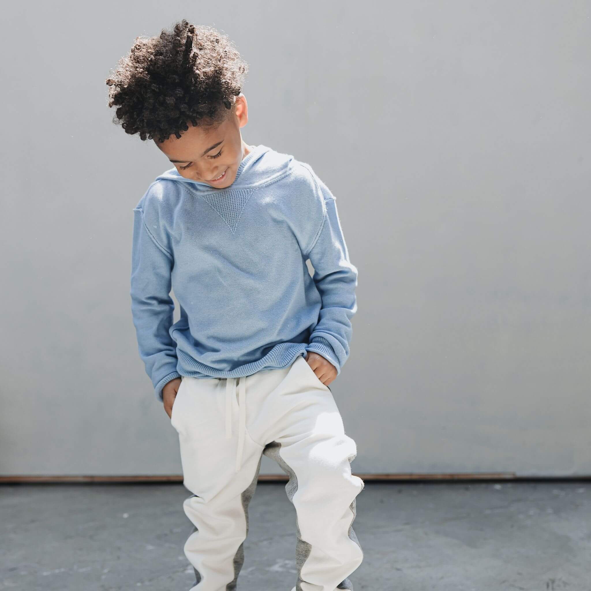 A boy wearing the Firebird Kids soft blue cotton-cashmere hoodie sweater and colorblock sweatpants