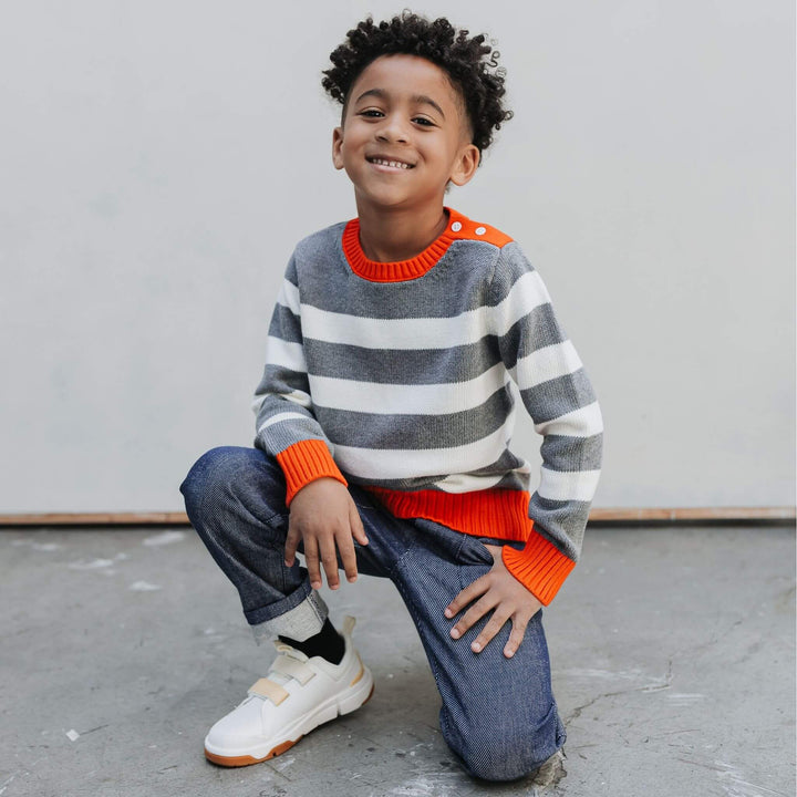 Boy seated in the Firebird Kids red-trimmed organic cotton striped crewneck sweater and denim pants