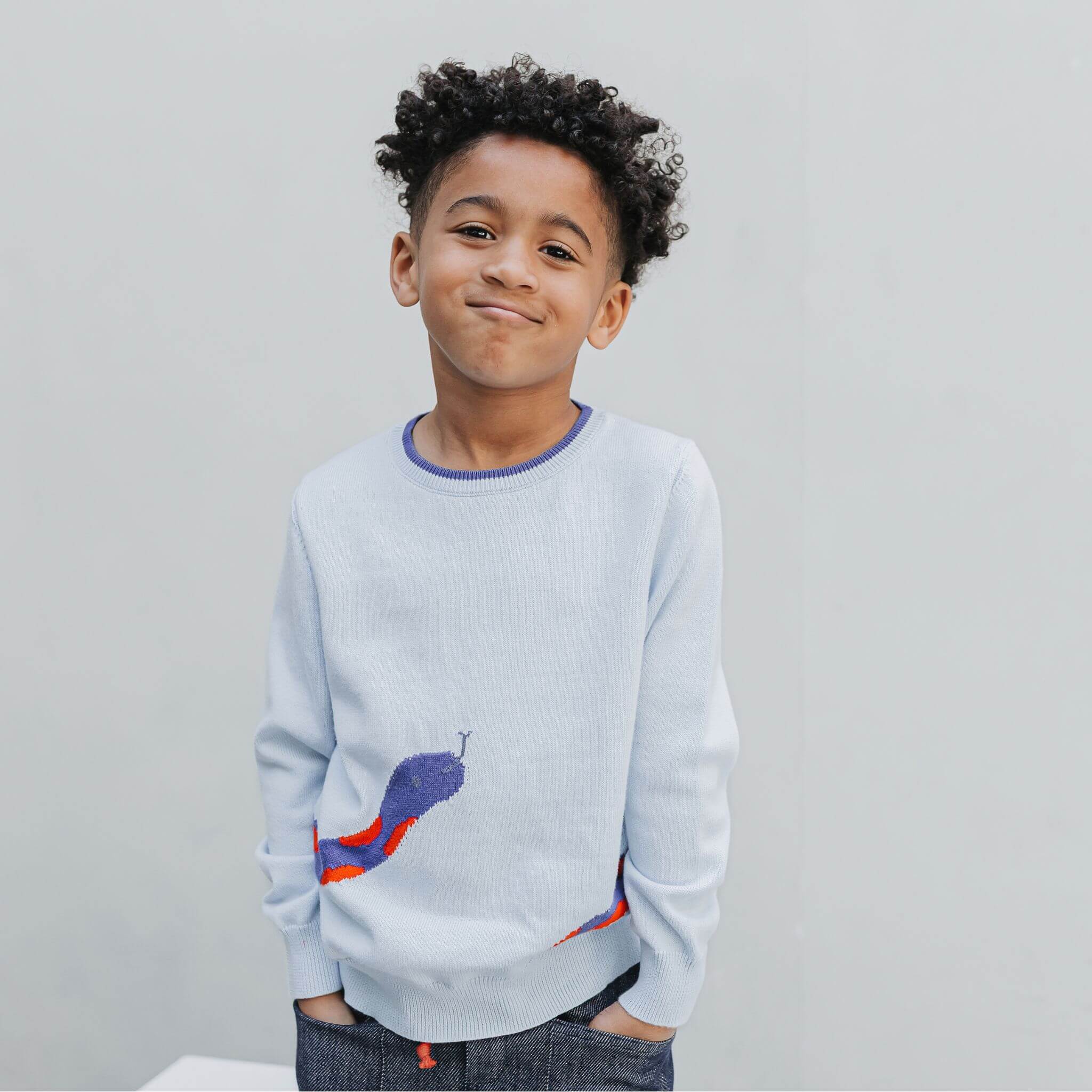 Boy standing in the unisex graphic sweater, snake head visible on the front of the powder blue organic cotton knit