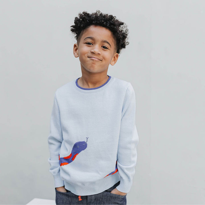 Boy standing in the unisex graphic sweater, snake head visible on the front of the powder blue organic cotton knit