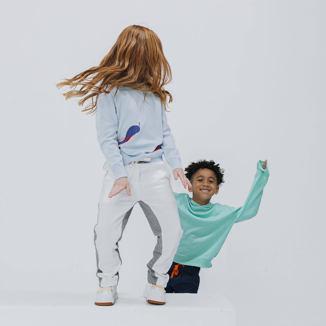 Girl in the powder blue snake sweater jumping beside a boy in a green sweater, Firebird Kids knitwear