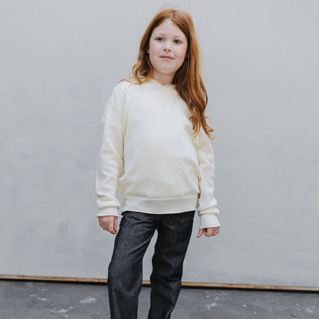 Front view of the Firebird Kids ivory cotton-cashmere hoodie sweater on a girl wearing denim pants