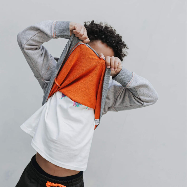 Boy pulling up a mockneck half zip sweatshirt to show the orange inside of the fabric 