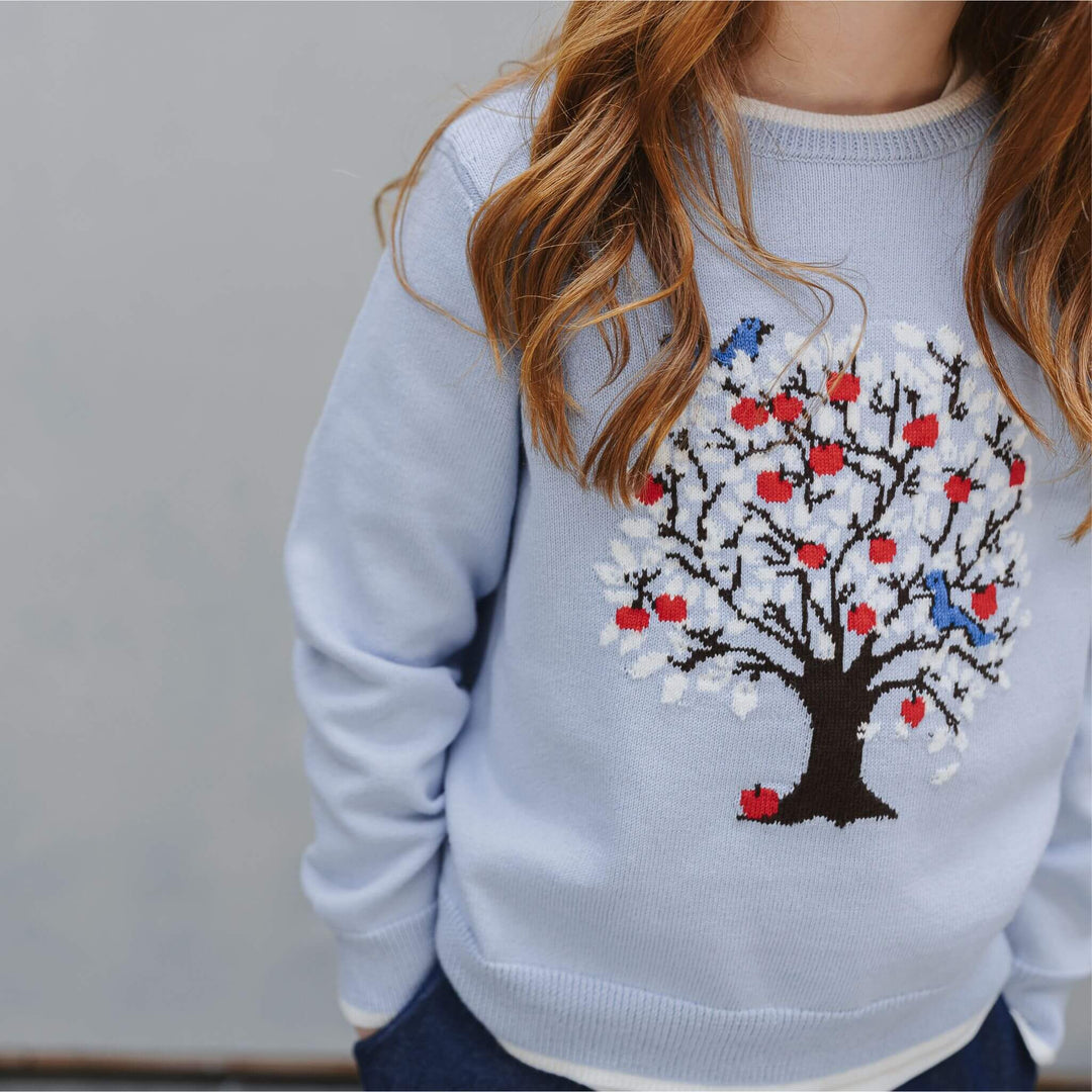 Front view of a girl wearing the blue sweater with a red, white and blue tree motif