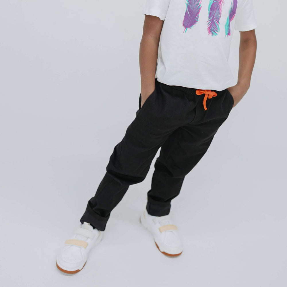Boy with hands in the front pockets of black drill pants, white graphic tee, cropped front view