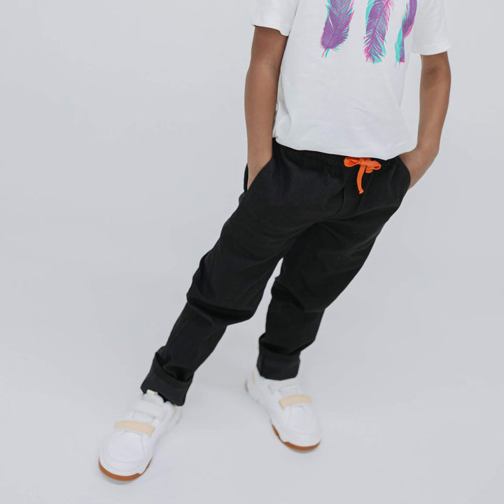 Boy with hands in the front pockets of black drill pants, white graphic tee, cropped front view