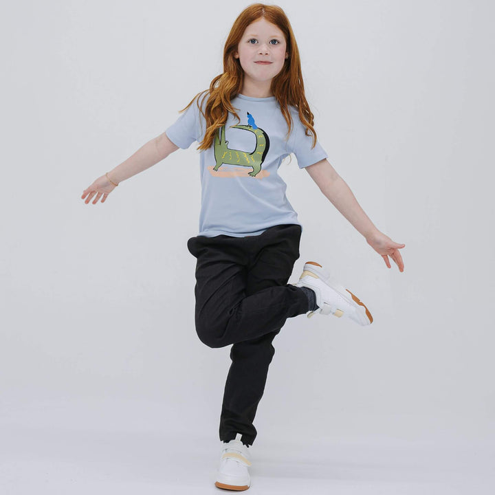 Girl dancing on one leg in black cotton drill pants and a light blue tee, showing how the pants move