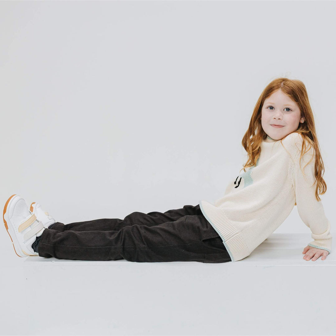 Girl lying on a white block wearing black Vintage Drill Pants and a cream sweater