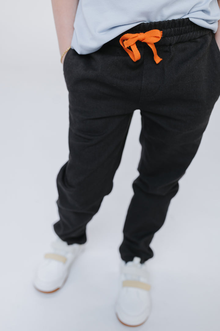 Firebird Kids Vintage Drill Pant in black, worn by a boy: covered elastic waistband, orange drawstring and straight leg