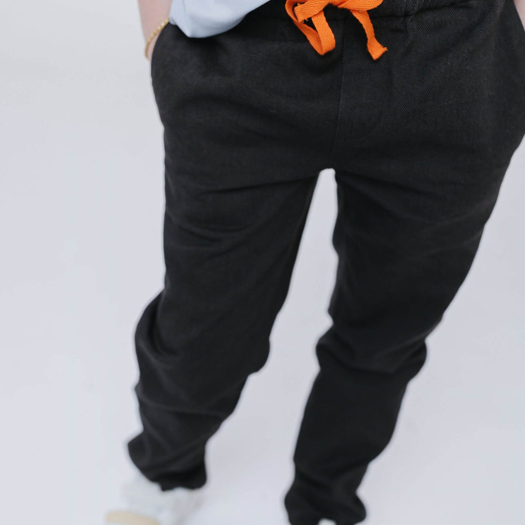 Close-up of the elastic waistband and orange drawstring on Firebird Kids' black Vintage Drill Pant, worn by a kid