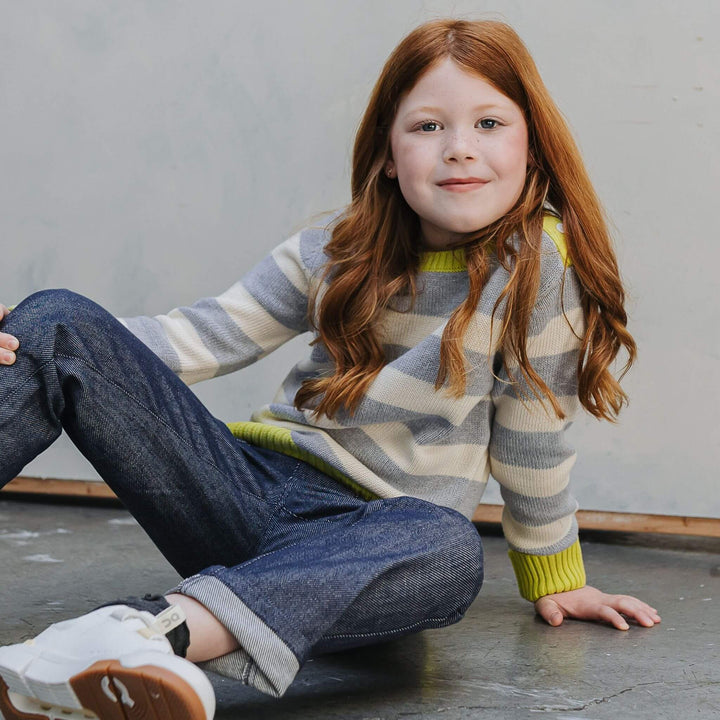 Girl wearing the Firebird Kids yellow and ivory striped organic cotton crewneck sweater and denim pants