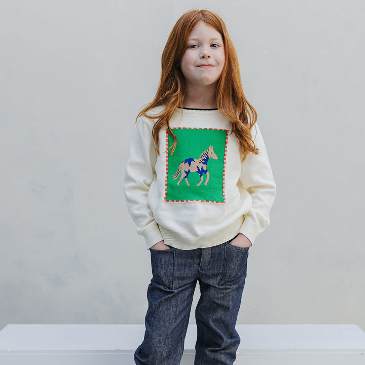 Girl standing in the Firebird Kids horse sweater and Studio Denim pants