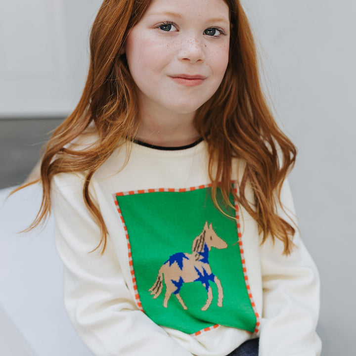 Close-up of the knitted-in intarsia horse panel with orange stitch border on the ivory organic cotton sweater