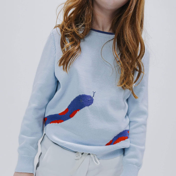 Girl wearing the Firebird Kids graphic sweater in powder blue with a violet snake knitted across the front