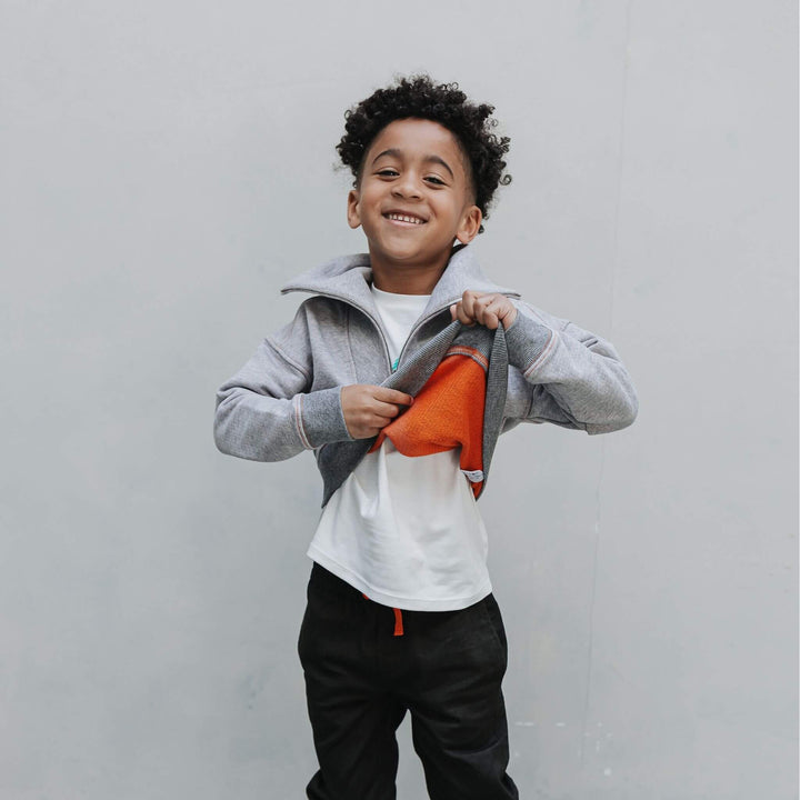 Boy pulling up a mockneck half zip sweatshirt to show the orange inside of the fabric 