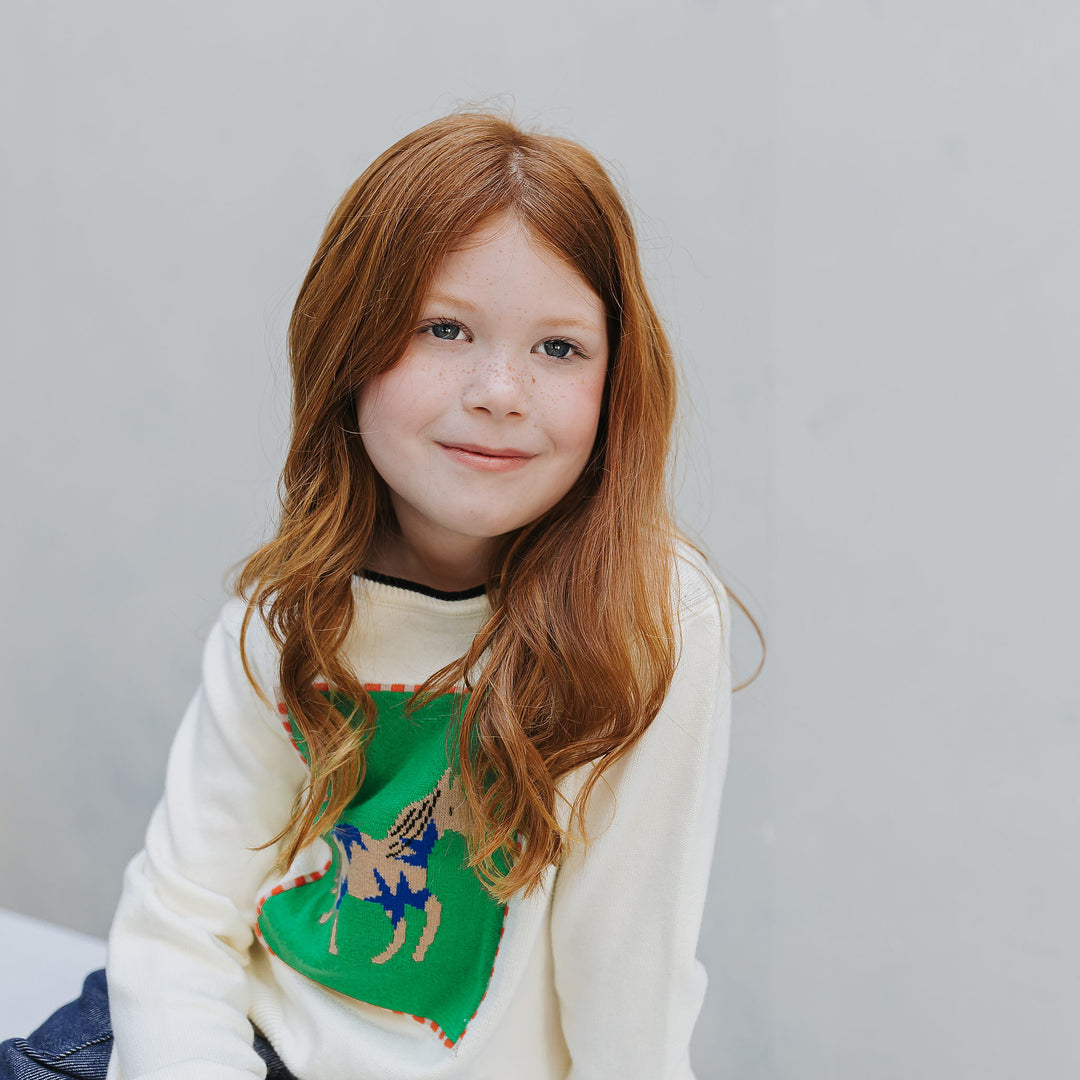Girl seated in the ivory organic cotton horse graphic sweater