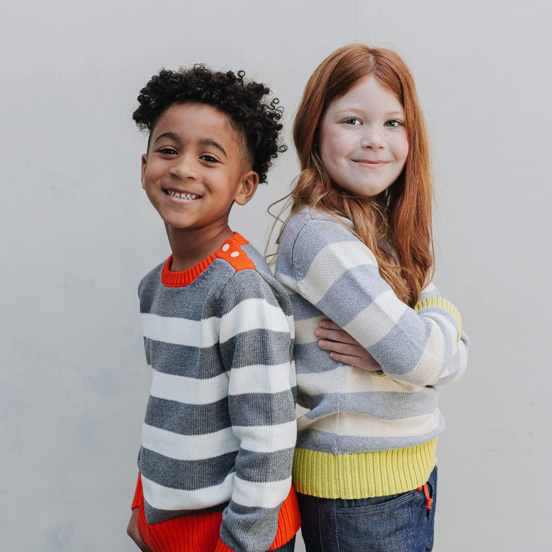 A boy and a girl wearing Firebird Kids organic cotton striped sweaters with yellow and red trim