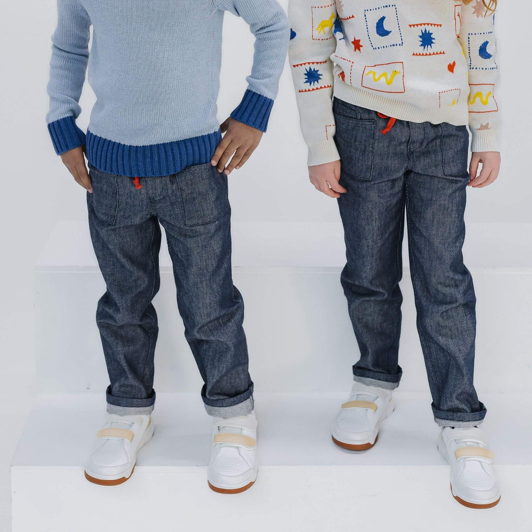 Two children standing side by side wearing dark blue soft denim jeans