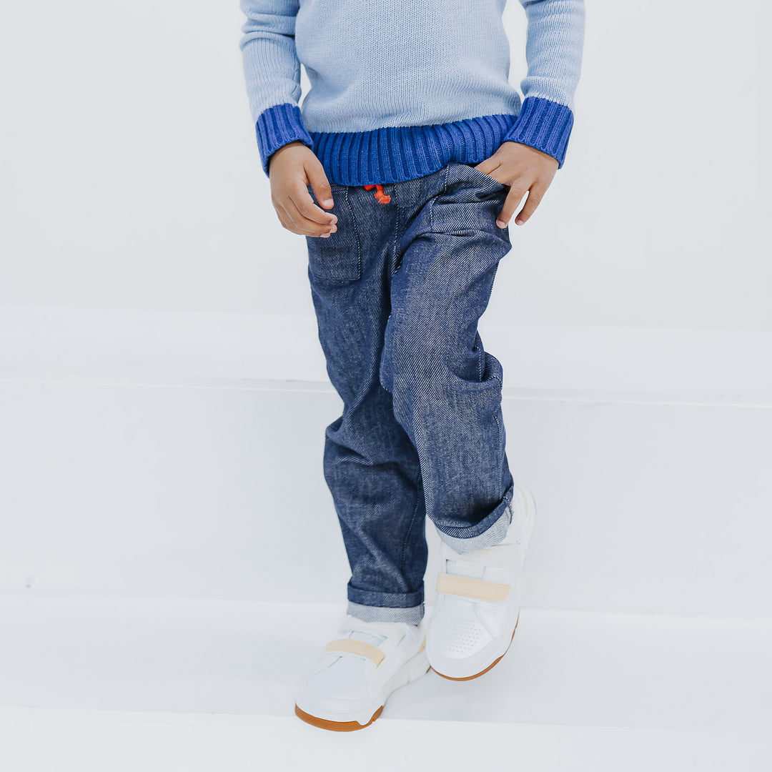 Firebird Kids Studio Denim Pant in navy organic Japanese denim with drawstring waist, worn with the light blue colorblock crewneck sweater