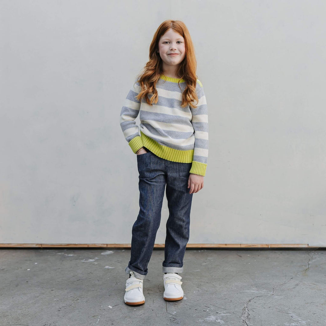 Girl wearing the Firebird Kids yellow and ivory striped organic cotton crewneck sweater and denim pants