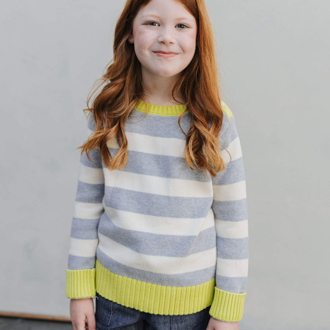 Girl wearing the Firebird Kids outfit of yellow and ivory striped organic cotton crewneck sweater and denim pants 