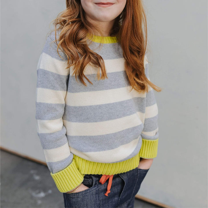 Girl wearing the Firebird Kids outfit of yellow and ivory striped organic cotton crewneck sweater and denim pants Girl wearing the Firebird Kids outfit of yellow and ivory striped organic cotton crewneck sweater and denim pants 