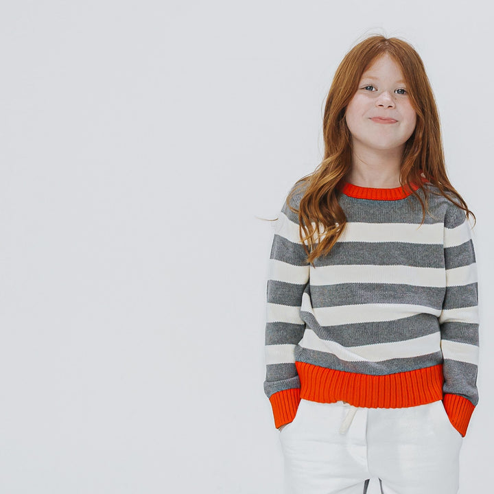 Girl wearing a red gray and white striped organic cotton sweater 