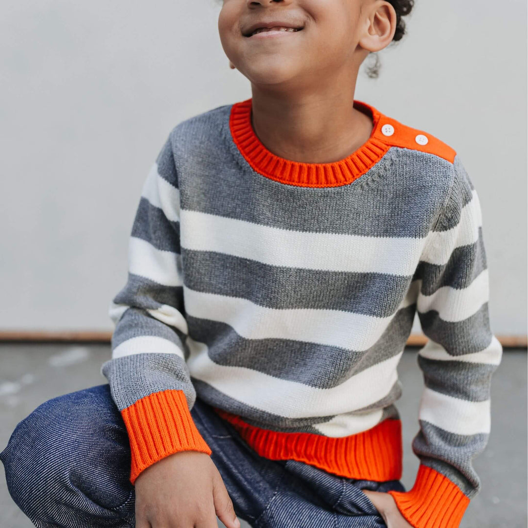 Child seated in the Firebird Kids red-trimmed organic cotton striped crewneck sweater
