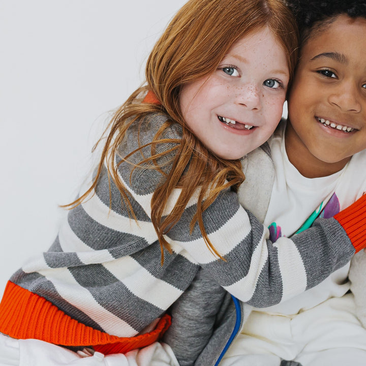 Girl wearing a red gray and white striped organic cotton sweater hugging a boy