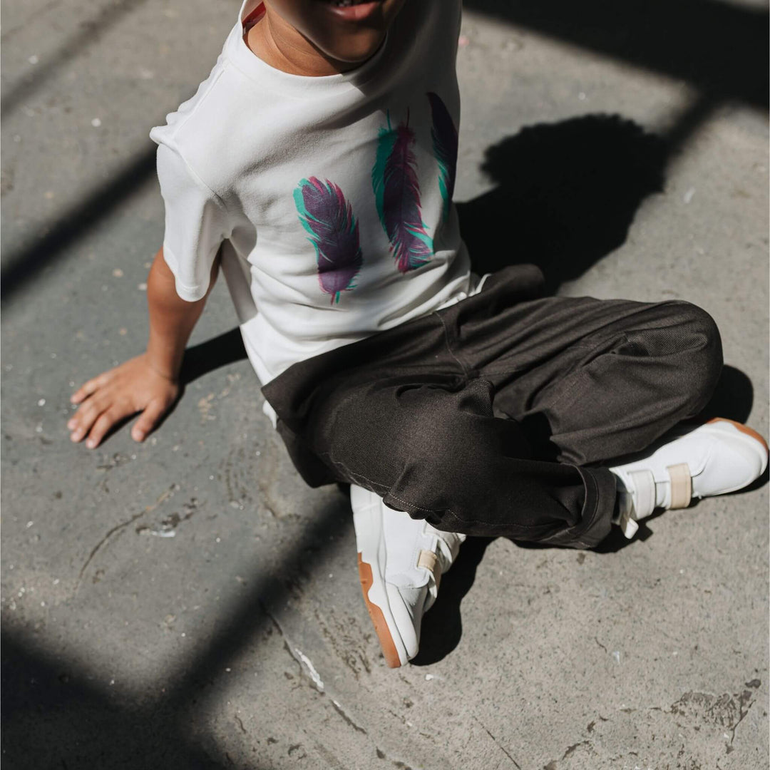 Child wearing a white organic cotton feather graphic tee with black pants