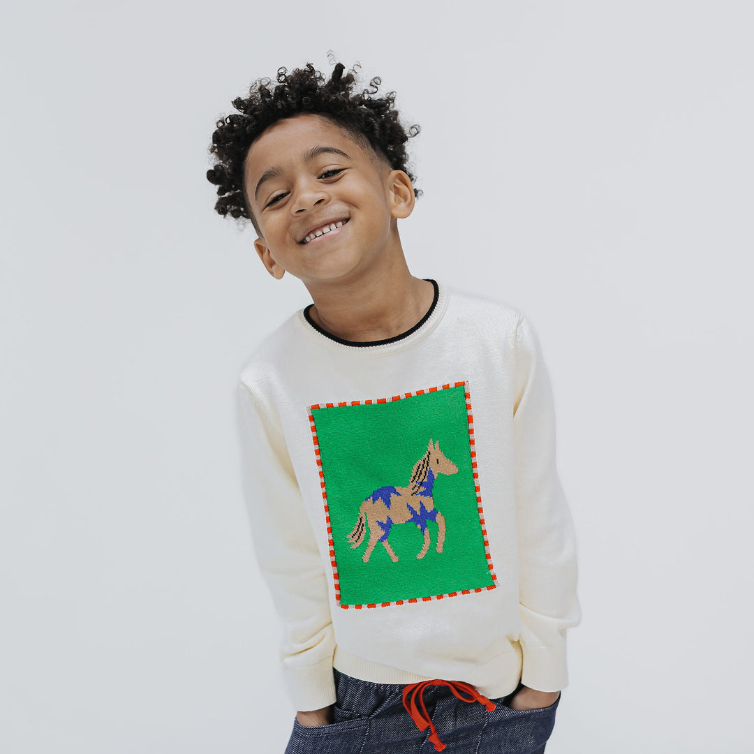 Boy smiling in the Firebird Kids Horse Intarsia Sweater, ivory organic cotton with a paint horse on a green panel