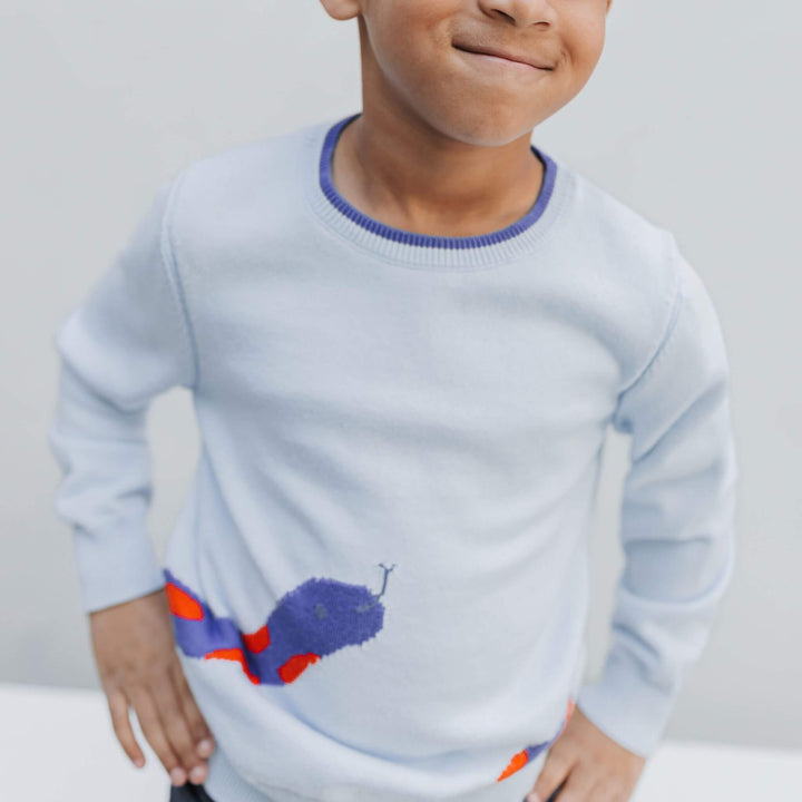Boy with hands on hips wearing the Firebird Kids snake sweater, violet and red intarsia snake at the hem