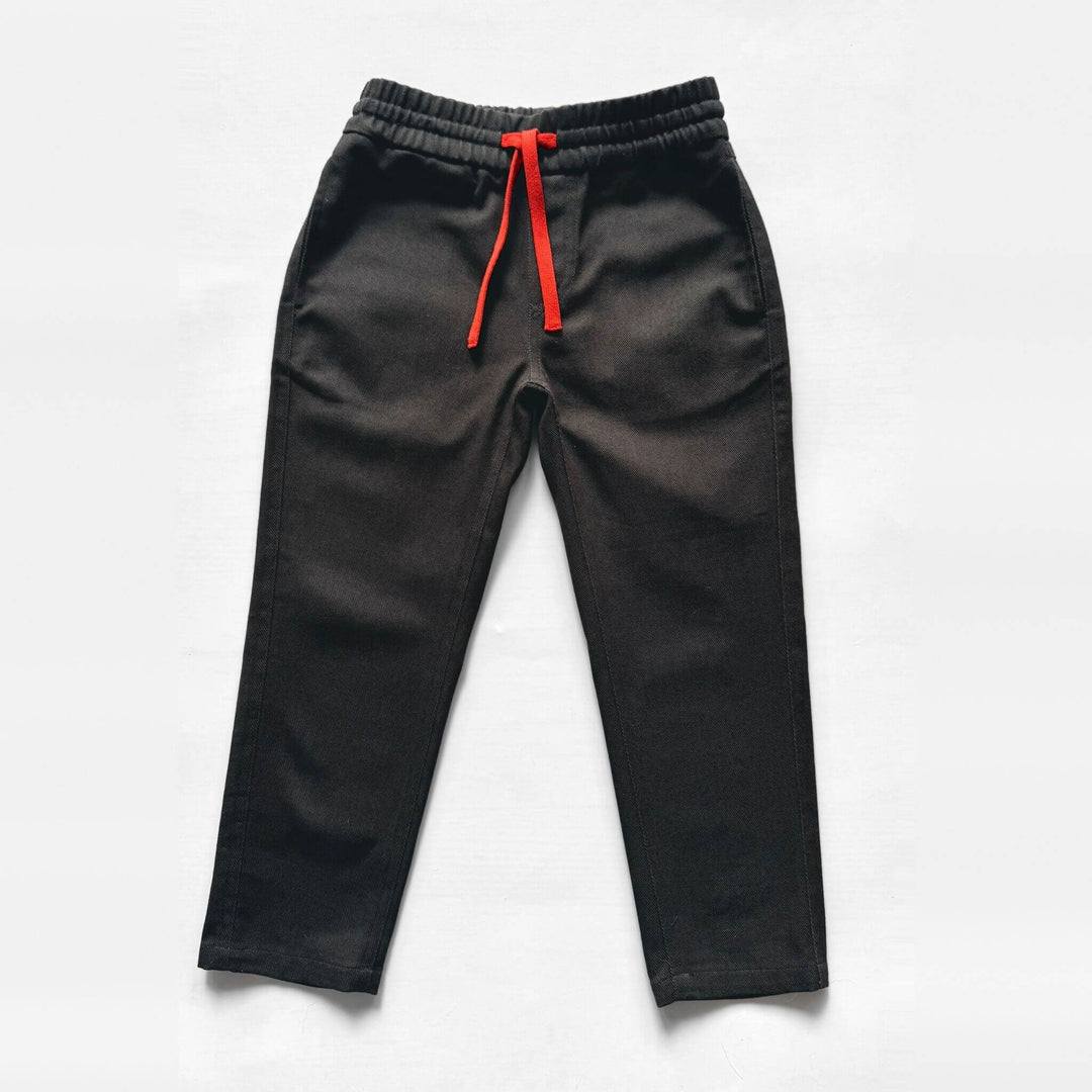 Flat lay of Firebird Kids' black Vintage Drill Pant with elastic waist and orange drawstring, front view