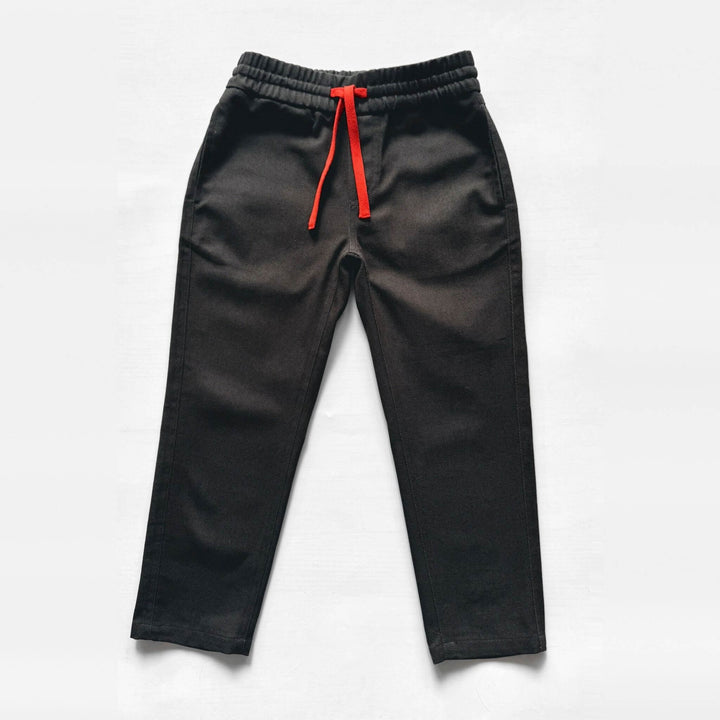 Flat lay of Firebird Kids' black Vintage Drill Pant with elastic waist and orange drawstring, front view