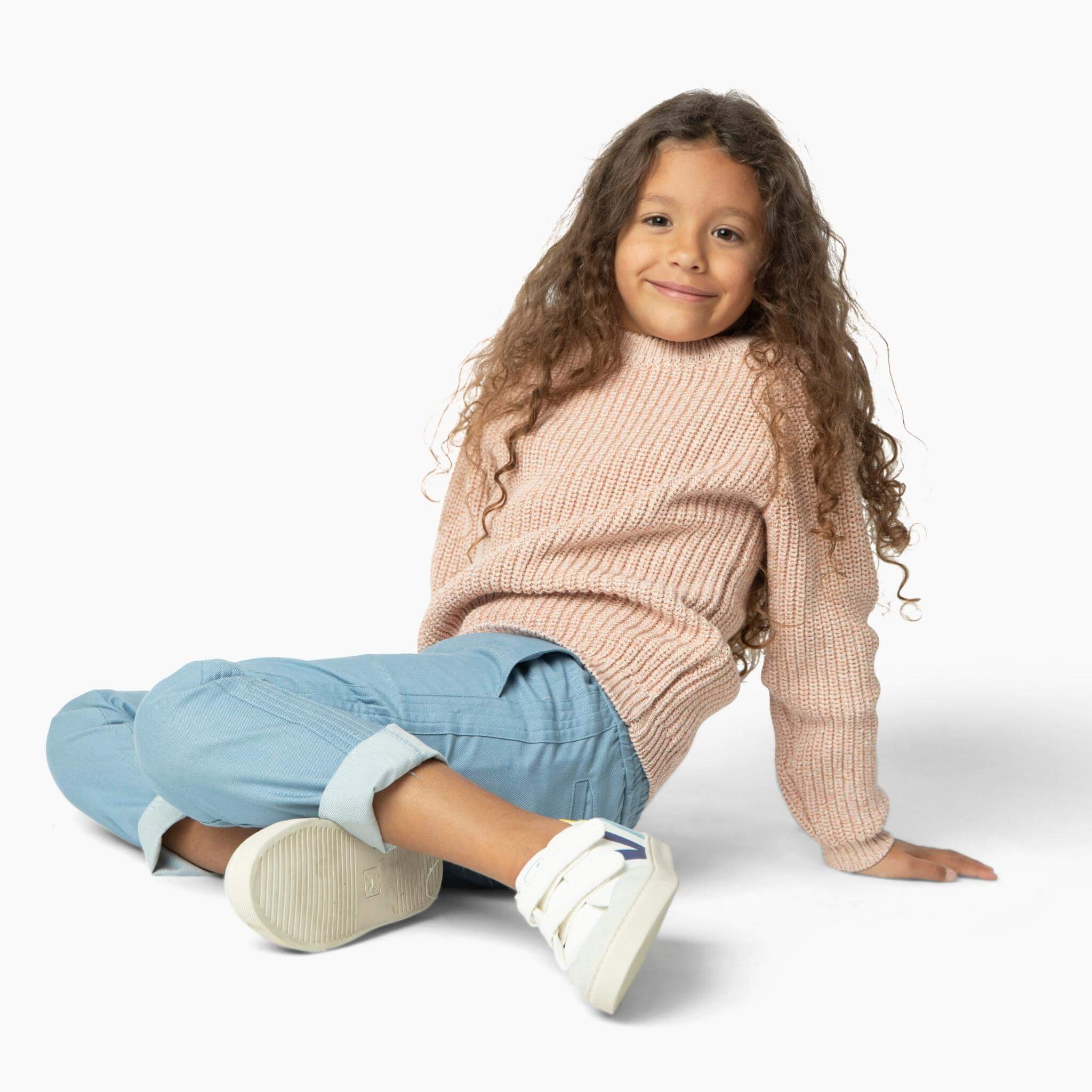 Girl wearing light blue soft denim pants and one of our best selling girls sweaters from our Kids Essentials collection. It is a chunky sweater made of organic Italian cotton yarn and is blush pink. 
