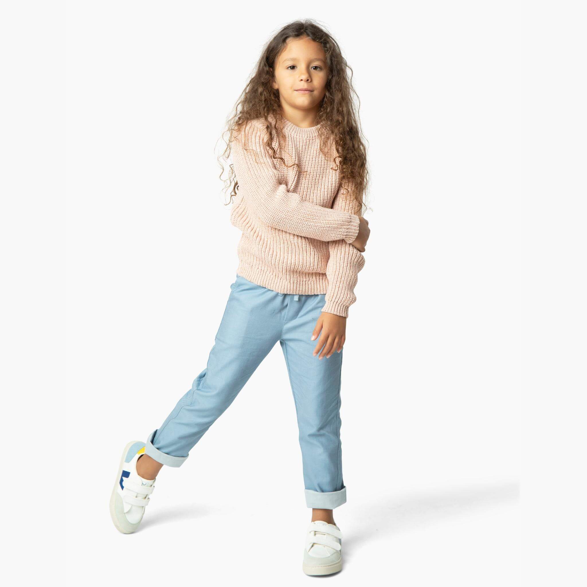 Girl wearing light blue soft denim pants and one of our best selling girls sweaters from our Kids Essentials collection. It is a blush, chunky sweater made of organic Italian cotton yarn.